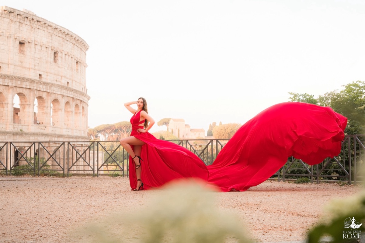 Posa flying dress The Icon: una mano tra i capelli e strascico rosso che disegna un arco, Colosseo all'alba, Roma