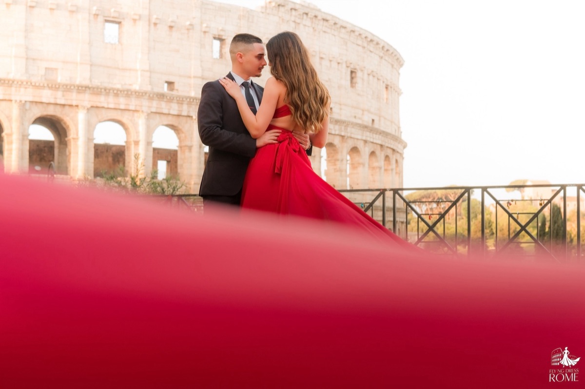 Posa flying dress di coppia The Tender Moment: coppia fronte contro fronte con il tessuto rosso sfocato in primo piano, Colosseo, Roma