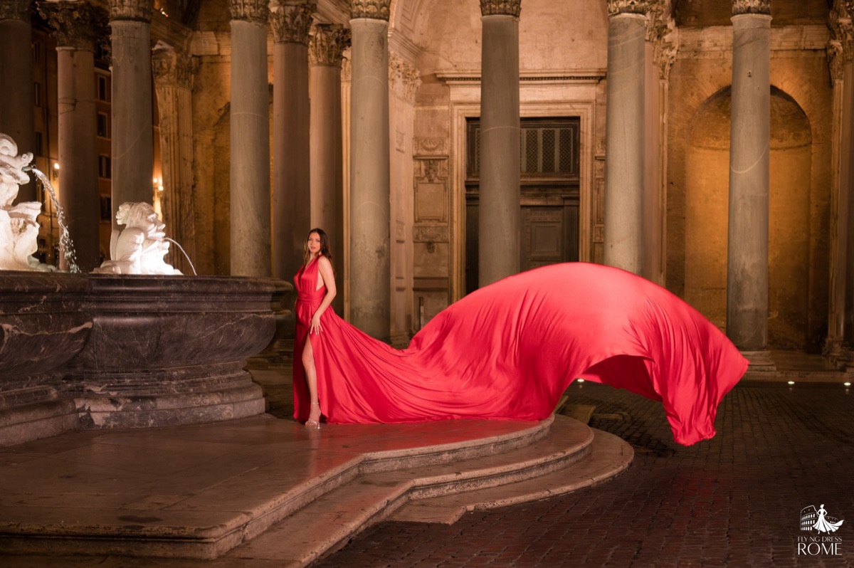 Posa flying dress The Stillness: figura ferma accanto alla fontana mentre lo strascico rosso si apre nel buio, Pantheon illuminato di notte, Roma
