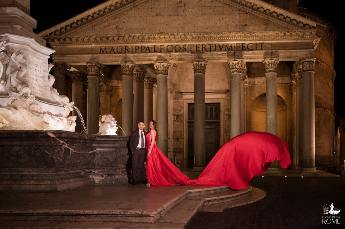 Posa flying dress di coppia The Classic: coppia in piedi davanti al Pantheon illuminato di notte con lo strascico rosso che vola, Roma